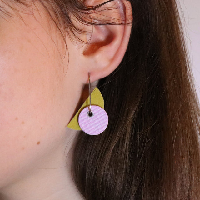 Close-up of a person wearing a colorful earring with a pink circle and yellow triangle.