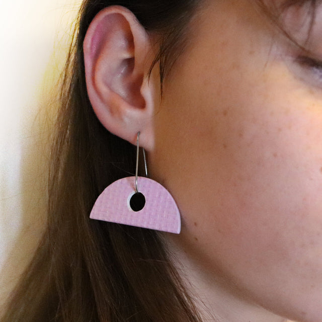 Close-up of a pink geometric earring worn by a person.