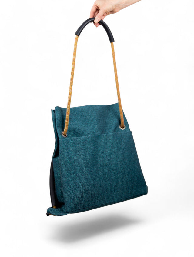 teal convertible bag held at top in front of white background