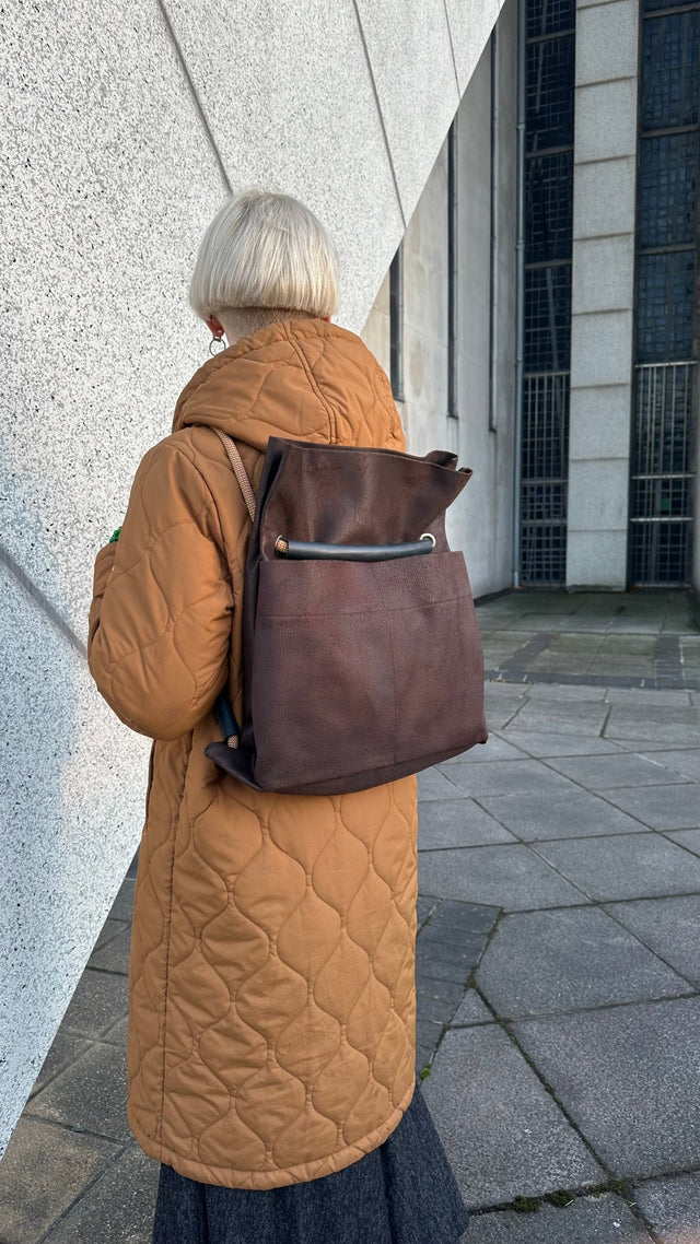 Brown Ditto backpack modelled by blond wearing orangish brown coat