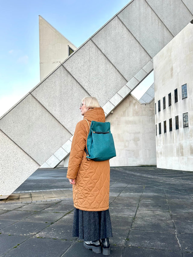 Teal Ditto backpack modelled by blond wearing orangish brown coat