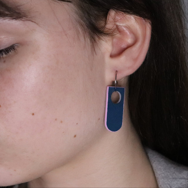 Close-up of an ear wearing a navy blue and pink earring made of linoleum