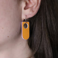 Close-up of a person wearing a orange and lilac earring made from recycled linoleum 