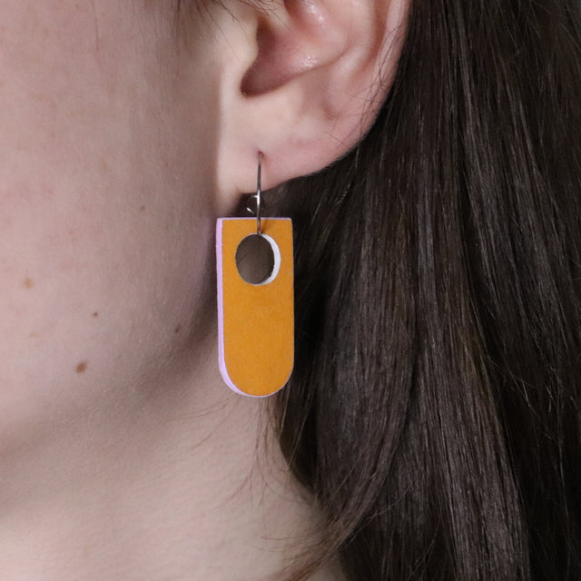 Close-up of a person wearing a orange and lilac earring made from recycled linoleum 