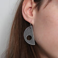Close-up of a person wearing a grey geometric earring against a neutral background