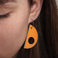 Close-up of a person wearing an orange teardrop-shaped earring.