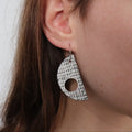 grey and white textured d shaped earring worn by brunette
