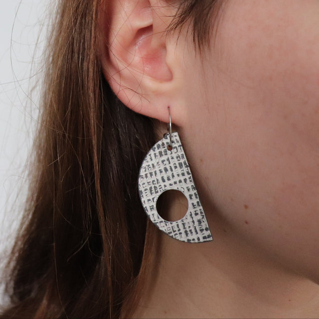 grey and white textured d shaped earring worn by brunette