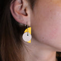 Close-up of a person wearing a yellow and white textured earring.
