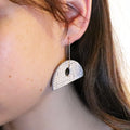 Silver earrings worn by a person with dark hair.