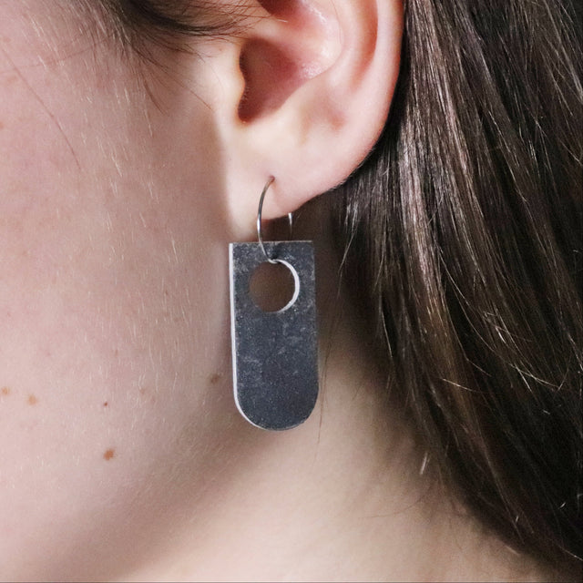 Close-up of a person wearing a grey and white arch pendant earring on hoop