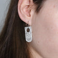Earring worn by a person with dark hair, against a neutral background
