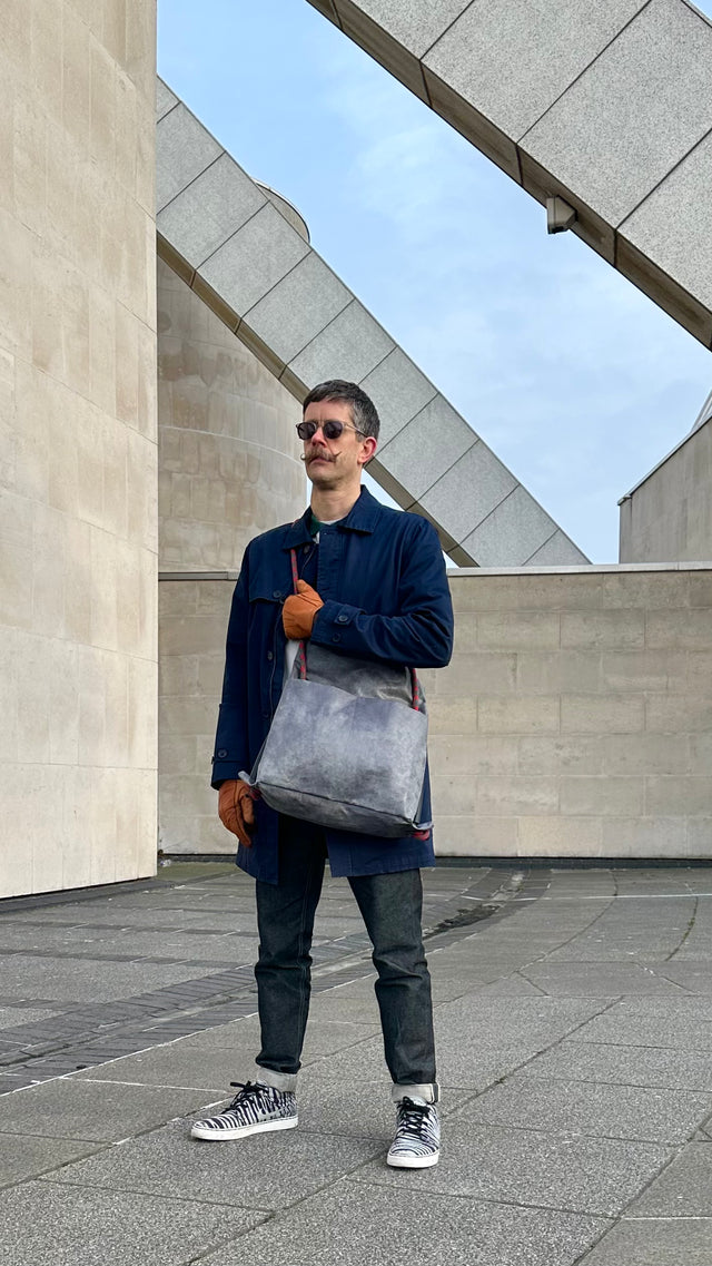 Man holding a gray bag outdoors with architectural background