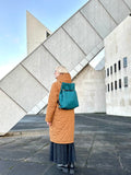 Teal Ditto backpack modelled by blond wearing orangish brown coat